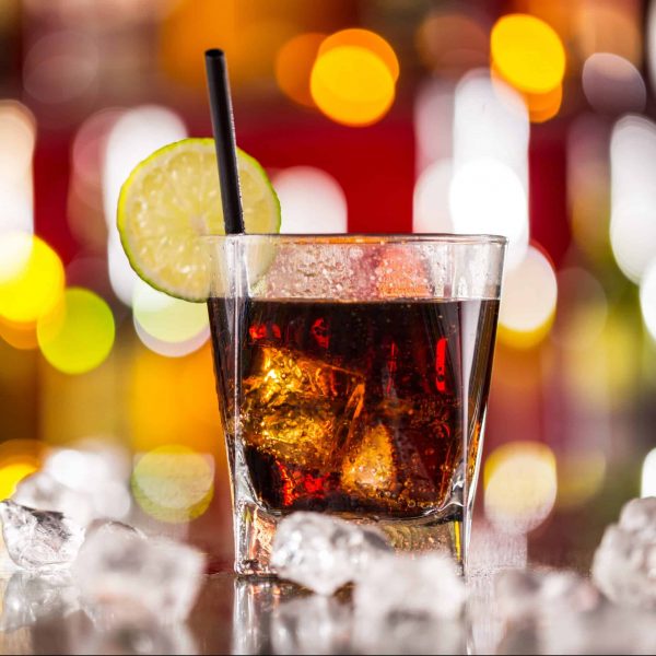 Glass of cola drink on bar counter with ice cubes